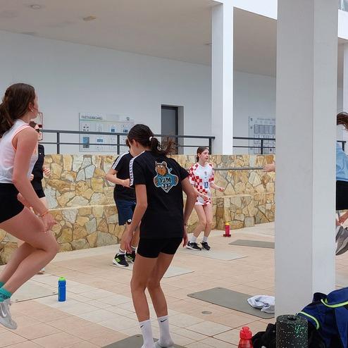 Gruppenübungen von Mädchen und Jungen in Sportkleidung in einem Trainingsbereich mit Steinen und Wasserflaschen.