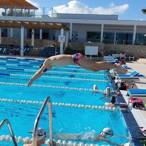 Ein Schwimmer springt kopfüber von einem Startblock in ein Freibadbecken mit mehreren Bahnen.