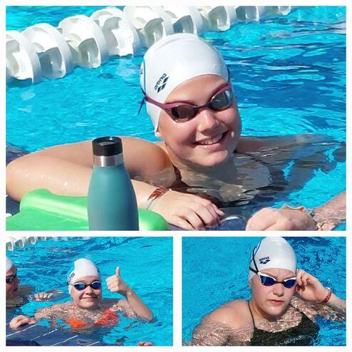 Junge Schwimmerin mit Badekappe lächelt am Beckenrand, neben ihr steht eine Wasserflasche auf der grünen Matte.