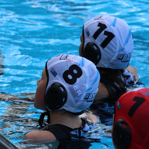 Nahaufnahme von Wasserballspielern mit wei&szlig;en Badekappen, Schwimmen im blauen Becken. Spieler mit den Nummern 7, 8 und 11.