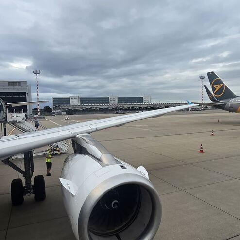 Blick auf das Vorfeld eines Flughafens mit zwei Flugzeugen und einem Bodenpersonal vor dem Triebwerk.