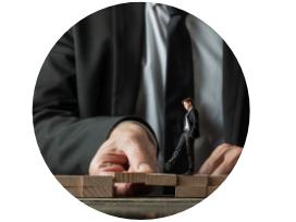 Ein kleiner Mensch im Anzug steht auf einem Holzbrett, während eine Hand das Brett stützt.