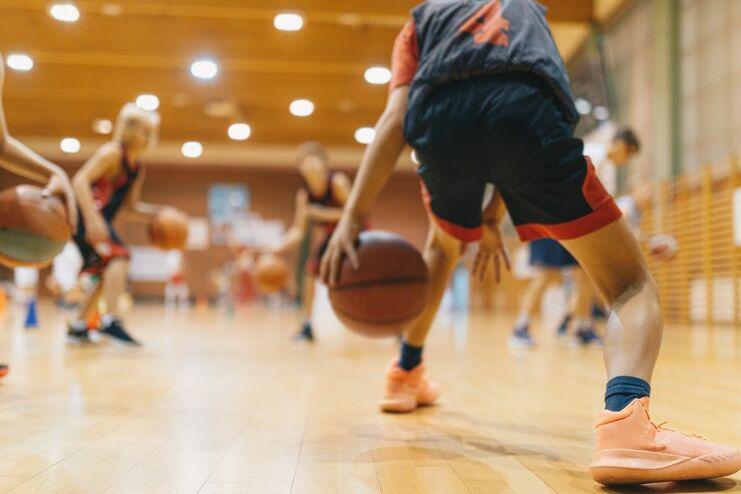 Jugendliche trainieren in einer Sporthalle, während sie Basketball dribbeln und an ihren Techniken arbeiten.