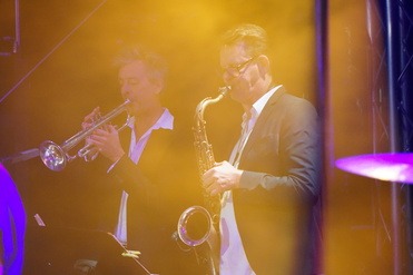 Zwei Musiker spielen im Bühnennebel Trompete und Saxophon bei einem Live-Auftritt.