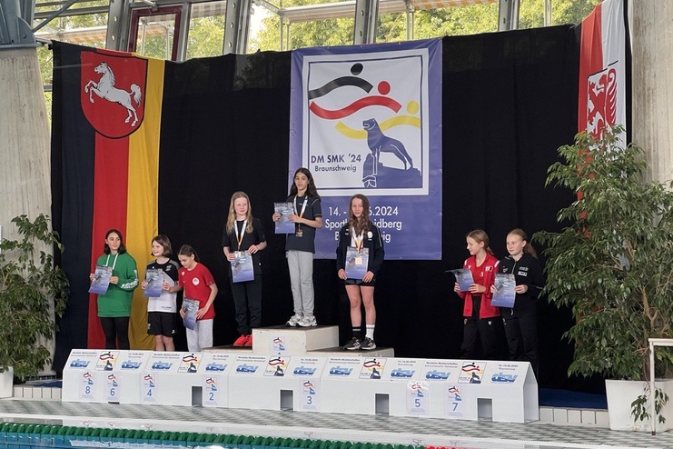 Siegerpodest mit Medaillengewinnern bei der DM SMK ’24, umgeben von Flaggen und einer großen Banner.