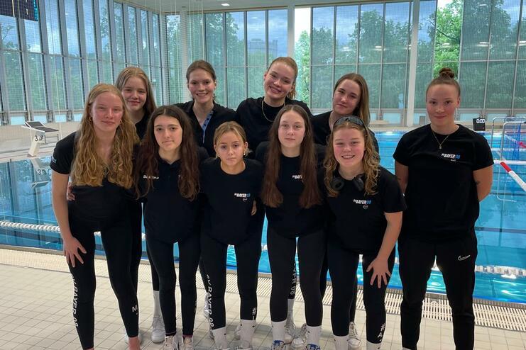 Gruppe von zehn Mädchen in schwarzen T-Shirts und Leggings, posierend am Beckenrand eines Schwimmbades.