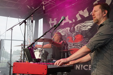 Zwei Musiker spielen live auf einer Bühne; ein Schlagzeuger und ein Keyboarder im Vordergrund.