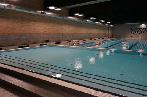 Innenansicht eines Schwimmbeckens mit Sprungbrettern und blauer Wasseroberfläche in einem modernen Hallenbad.