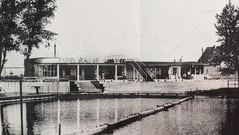 Historisches Schwarz-Weiß-Bild eines Gebäudes am Wasser mit Treppe und Garten, umgeben von Bäumen.