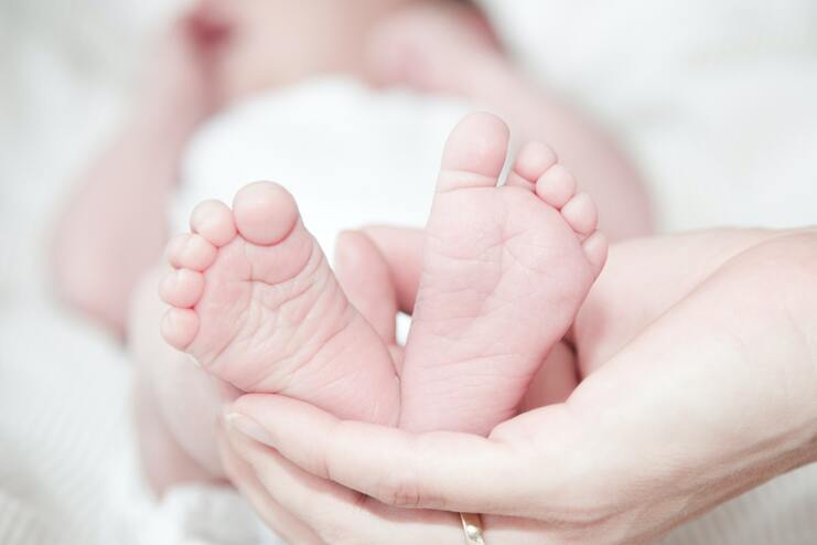 Nahaufnahme von Babyfüßen, die in einer Hand gehalten werden, vor unscharfem Hintergrund.