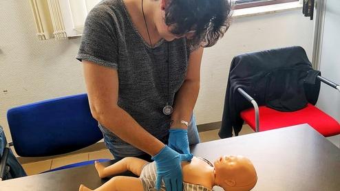 Eine Person in blauen Handschuhen führt Erste-Hilfe-Maßnahmen an einer Baby-Puppe auf einem Tisch aus.