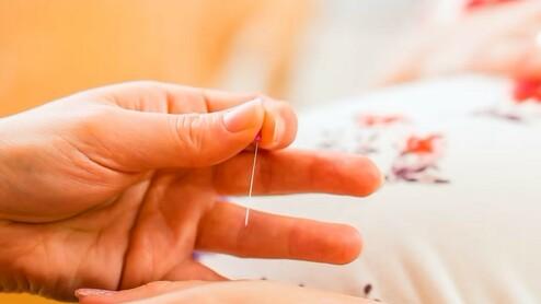 Nahaufnahme von einer Hand, die eine Nadel hält, während sie über einen bauchigen, blumigen Stoff gleitet.