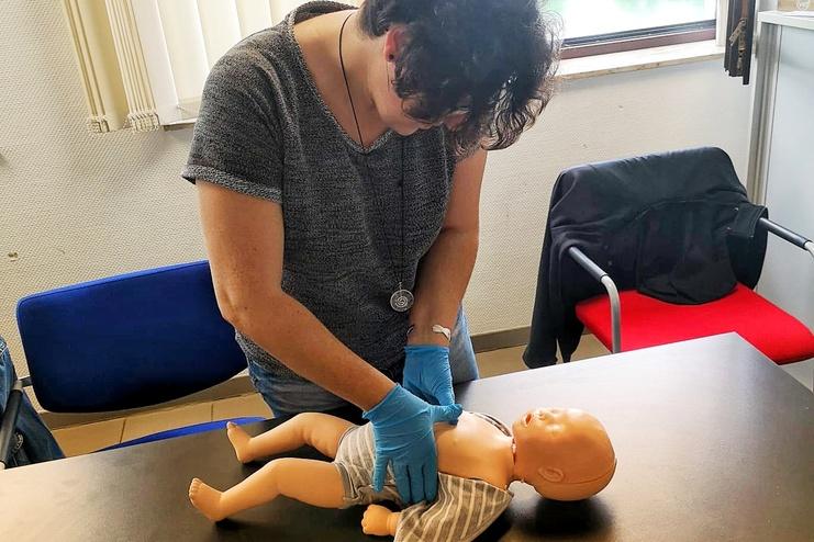 Eine Person in blauen Handschuhen führt Erste-Hilfe-Maßnahmen an einer Baby-Puppe auf einem Tisch aus.