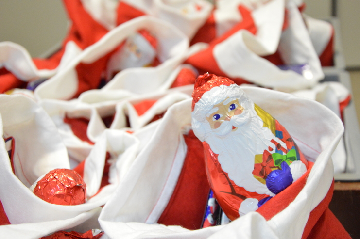 Lebkuchenfiguren und Schokoladenweihnachtsmann in roten und weißen Tüten auf einem Tisch.