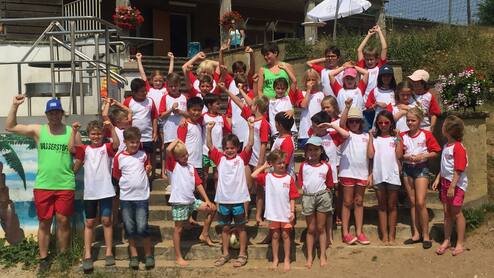 Gruppenfoto von Kindern in weißen T-Shirts mit roten Ärmeln, die vor einem Gebäude am Strand stehen und feiern.