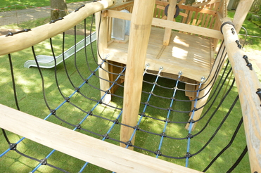 Klettergerüst aus Holz mit Seilnetz und Rutsche auf grünem Rasenteppich im Freien.