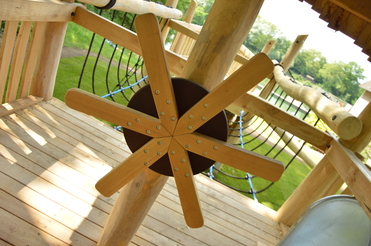 Detailansicht eines Holzspielgeräts mit einem rotierenden Rad aus Holz und Stricknetz im Hintergrund.