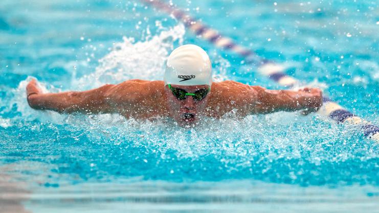 Ein Schwimmer in einem weißen Badekappe und grünen Schw goggles schwimmt im Schmetterlingsstil durch das Wasser.