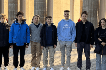 Gruppe von sieben Jugendlichen steht vor einer historischen Säulenfassade im Freien, alle tragen Freizeitkleidung.