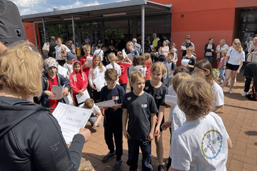 Gruppierung von Kindern und Erwachsenen bei einer Urkundenverleihung im Freien vor einem Gebäude.