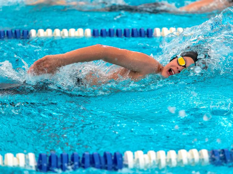 Ein junger Schwimmer in einem blauen Schwimmbecken vollbringt einen kraftvollen Kraul-Zug mit Wasser spritzend.