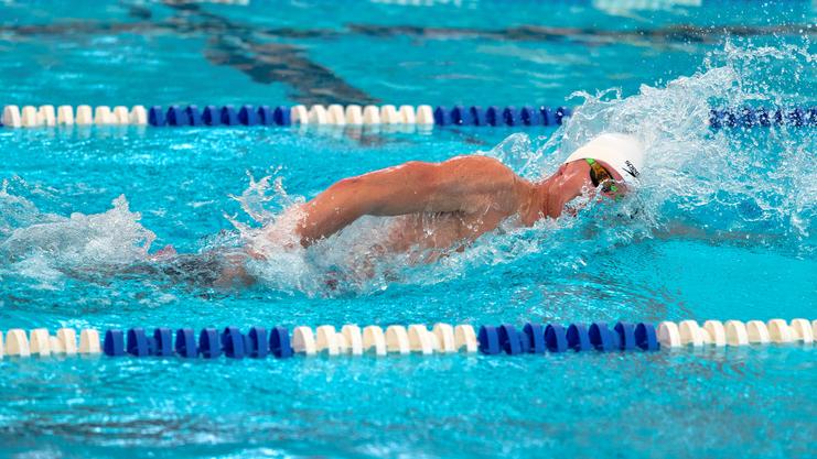 Schwimmer im weißen Badekappe schwimmt unterm Wasser auf einer blauen Schwimmbahn mit Spritzwasser.