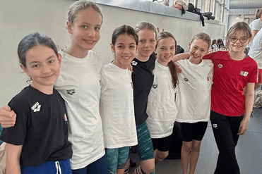 Gruppe von sechs Mädchen in Badeshirts und verschiedenen Socken steht nebeneinander in einem Schwimmbad.