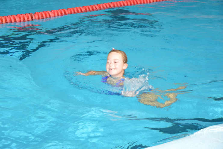 Lächelndes Mädchen schwimmt in einem Schwimmbecken, Wasser spritzt um sie herum.