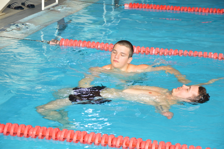 Zwei Jungen schwimmen im Wasser eines Schwimmbeckens, einer liegt entspannt auf dem Rücken.