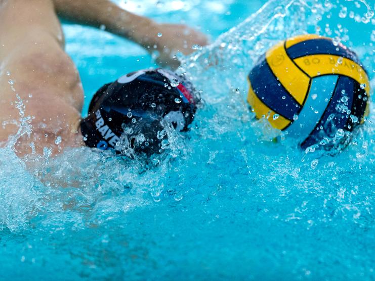 Spritzernde Wassertropfen w&auml;hrend eines Wasserball-Spiels mit zwei Spielern und einem Ball im Fokus.