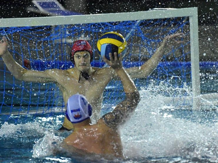 Wasserballspieler blockiert einen Wurf mit einem Ball in einem spritzenden Wasserbecken.