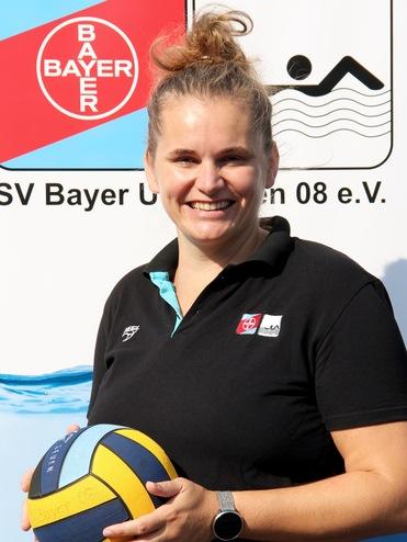 Frau mit Wasserball in der Hand steht vor einem Banner des SV Bayer Uerdingen 08 e.V. in einem sportlichen Outfit.