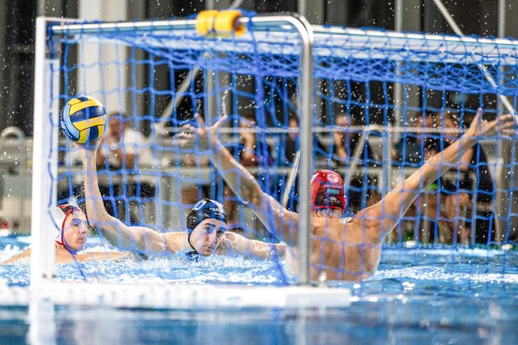 Wasserballspieler in Aktion: Ein Spieler wirft den Ball durch das Tor-Netz, w&auml;hrend Wasser spritzt.