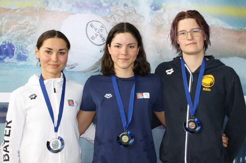 Drei Schwimmerinnen mit Medaillen stehen nebeneinander vor einer Wasser-Hintergrundgrafik.