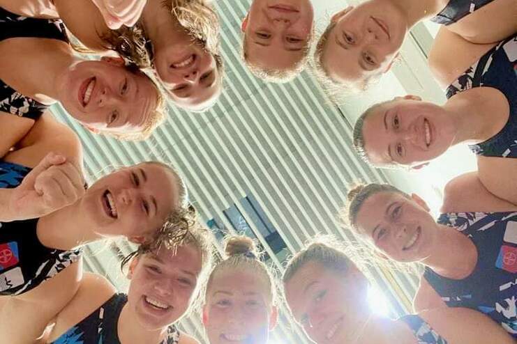 Gruppenfoto von zehn engagierten Schwimmerinnen in Sportanzügen, die lächeln und zusammen posieren.