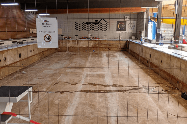 Leeres Schwimmbecken mit Absperrgitter und Hinweisschild "25m-Becken gesperrt" in einem Schwimmbad.