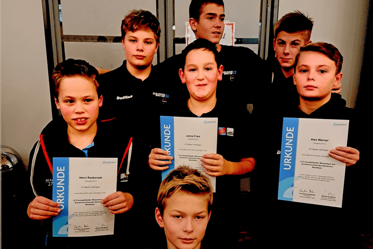 Gruppe von sieben Jugendlichen in dunkler Sportkleidung, die Urkunden für sportliche Leistungen halten.