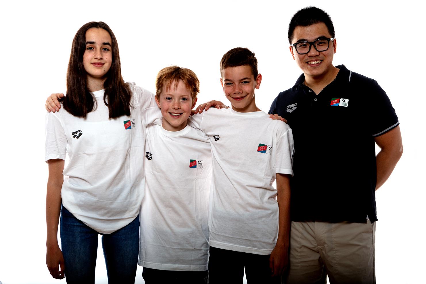 Vier Jugendliche stehen lächelnd in weißen T-Shirts mit Logo. Ein Junge trägt ein schwarzes Polohemd.