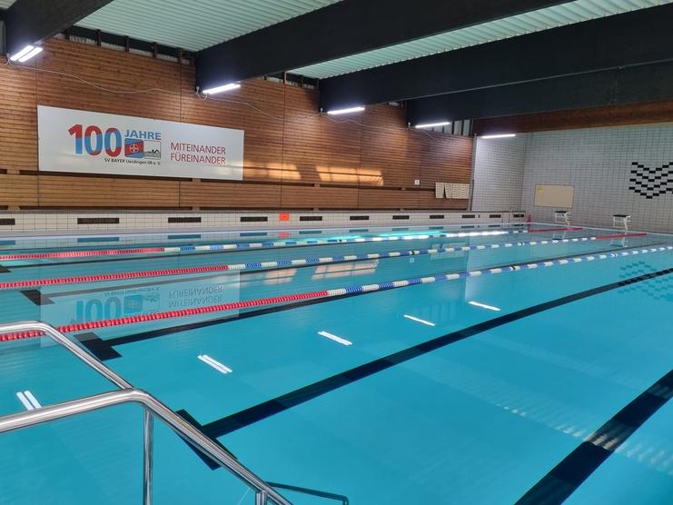 Innenaufnahme eines Schwimmbeckens mit blauen Wasser, farbigen Bahnen und einer Wand mit Jubiläumsbanner.