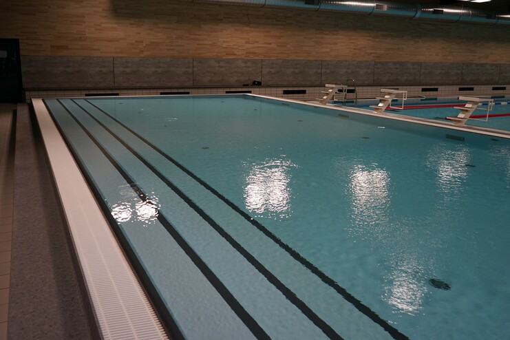 Schwimmbecken mit blauer Wasseroberfläche, gekennzeichnet durch schwarze Linien und eine Sprunganlage im Hintergrund.