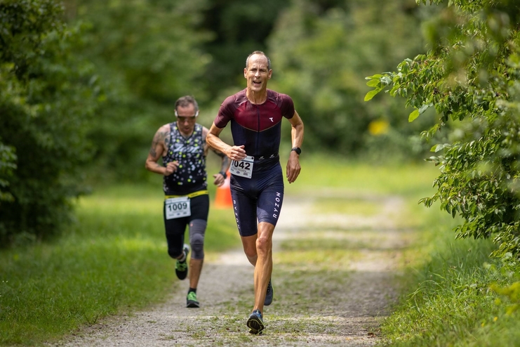 Zwei Athleten laufen auf einem Waldweg während eines Wettkampfs, einer trägt die Startnummer 1042, der andere 1009.