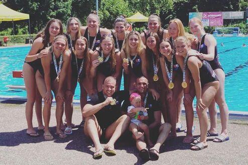 Gruppe von 15 Frauen in Sportkleidung mit Medaillen, umgeben von einem Schwimmbecken an einem sonnigen Tag.