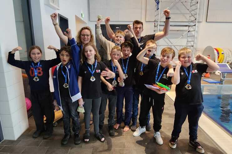 Gruppe von Kindern und Erwachsenen in Schwimmbekleidung, erfreut mit Medaillen und Siegerposen in einem Schwimmbad.