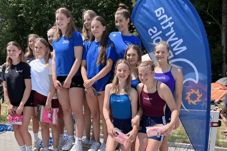 Gruppenshot von jungen Schwimmerinnen auf dem Siegerpodest bei einem Wettkampf, mit Medaillen und Preisen in der Hand.