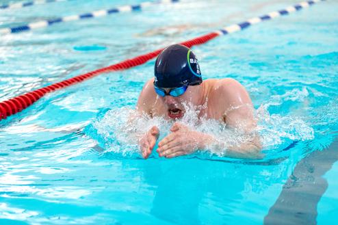 Schwimmer in blauer Badehose und Schwimmbrille führt einen Brustschwimmzug in einem Schwimmbecken aus.