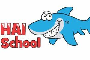 Grafik eines lächelnden blauen Haifischs neben dem Schriftzug „HAI School“ in roter Schrift.