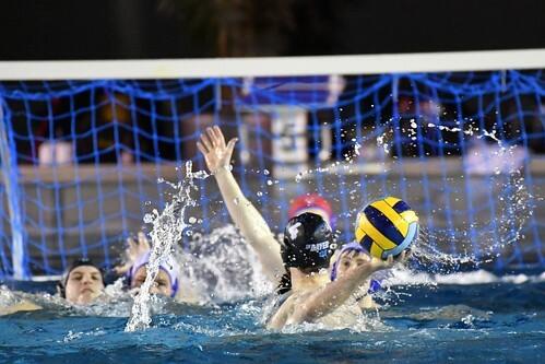 Wasserballspiel mit mehreren Spielerinnen, die um den Ball kämpfen und Spritzer im Wasser erzeugen.
