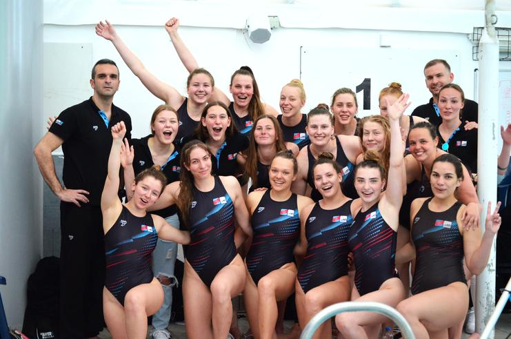 Gruppenfoto von Schwimmerinnen in schwarzen Badeanzügen, posierend mit einem Trainer, alle lächeln und haben Spaß.