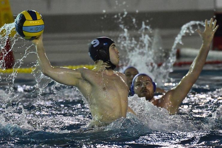 Wasserballer wirft einen Ball über spritzendes Wasser, während ein Gegenspieler versucht, ihn zu blockieren.