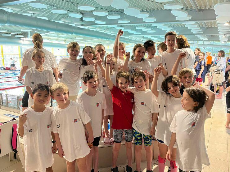 Gruppe von Kinder-Schwimmern in weißen T-Shirts, posierend mit sportlicher Begeisterung am Schwimmbecken.